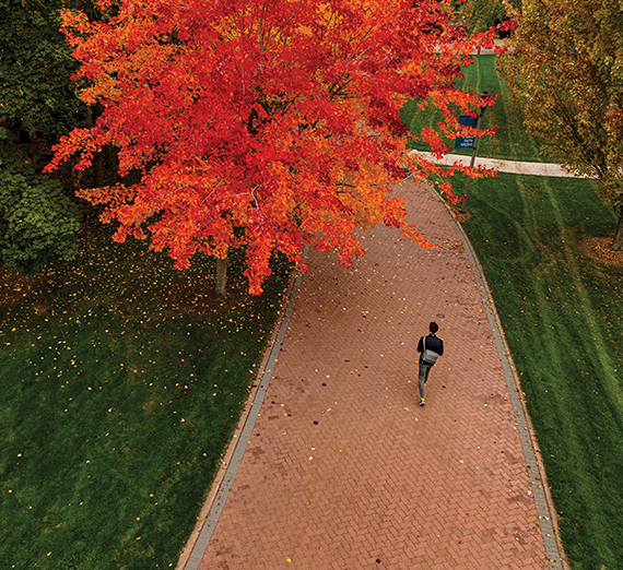 A female student in graduation cap and gown holds her degree over her head. 